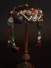 Load image into Gallery viewer, Full view of Upcycled vintage pillbox hat maximalized with heirloom mother-of-pearl buttons, silver Afghan clothing ornaments, antique Pashtun silver triangular ornaments and Afghani tent band tassels with silver.