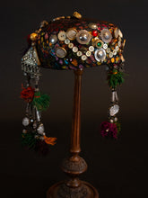Load image into Gallery viewer, Full view of Upcycled vintage pillbox hat maximalized with heirloom mother-of-pearl buttons, silver Afghan clothing ornaments, antique Pashtun silver triangular ornaments and Afghani tent band tassels with silver.
