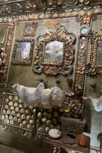 Load image into Gallery viewer, Side view of shell grotto powder room, walls and ceiling adorned with shells, shell-framed mirrors, shell dioramas, and giant clamshell sinks.
